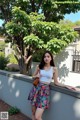 A woman leaning against a wall with a tree in the background.